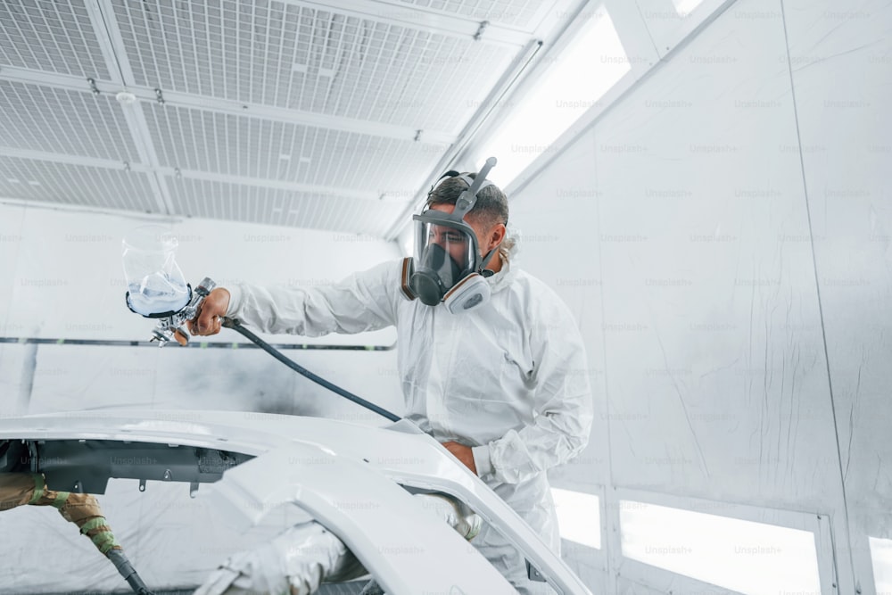 In protective mask. Painting the car. Caucasian automobile repairman in uniform works in garage.