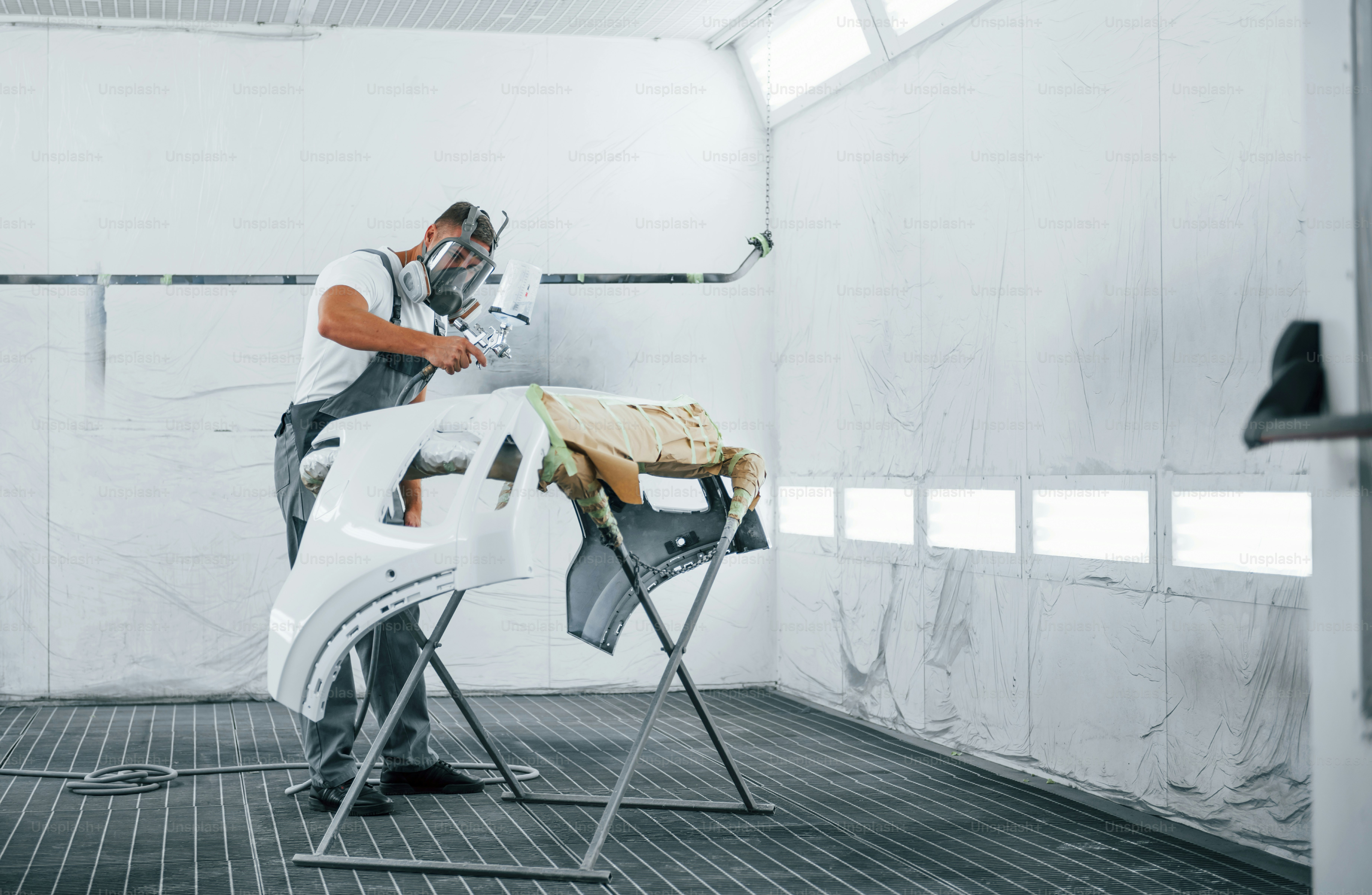 Uses painting gun. Caucasian automobile repairman in uniform works in garage.