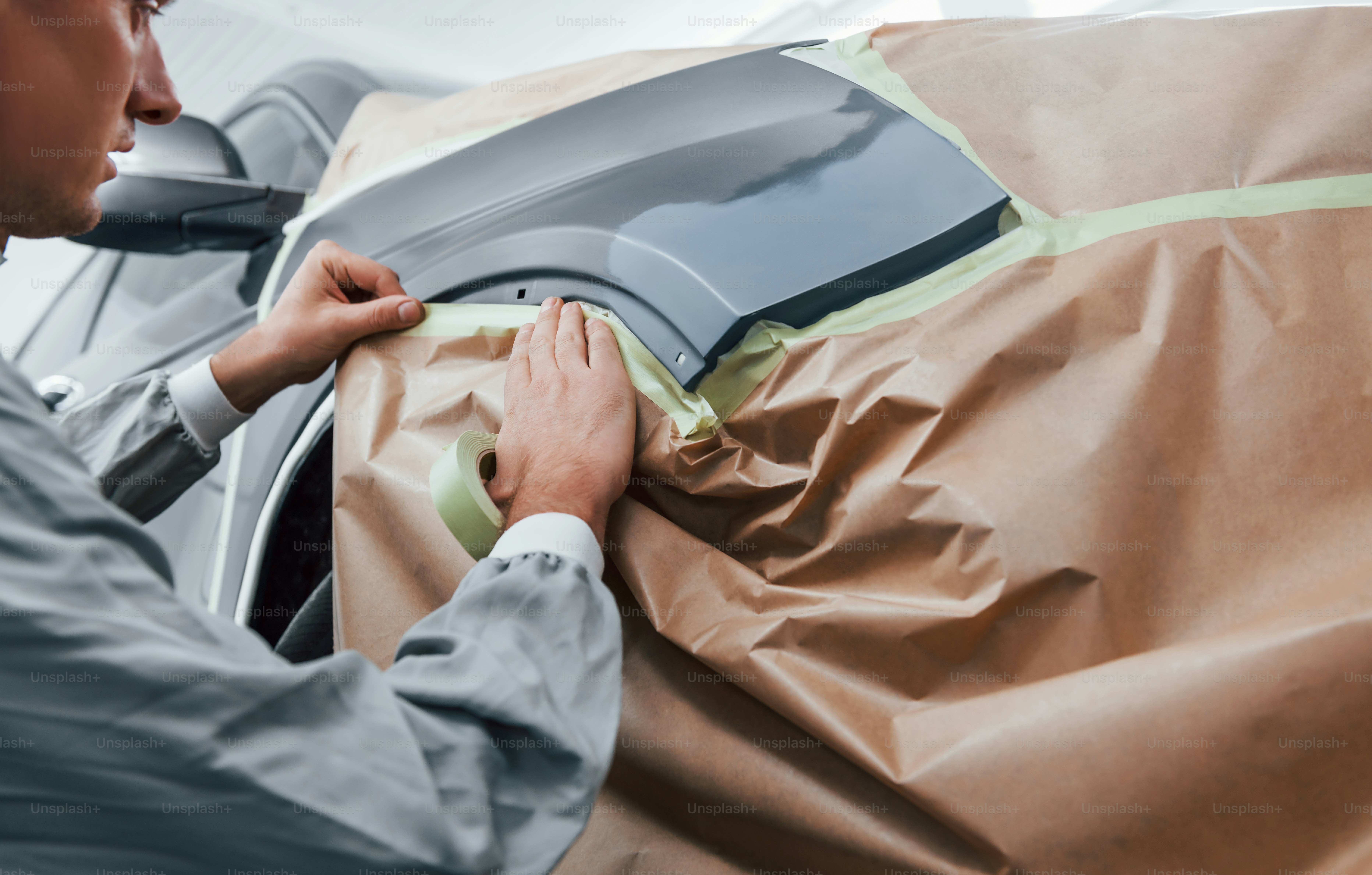 Covering car by brown cloth. Caucasian automobile repairman in uniform works in garage.