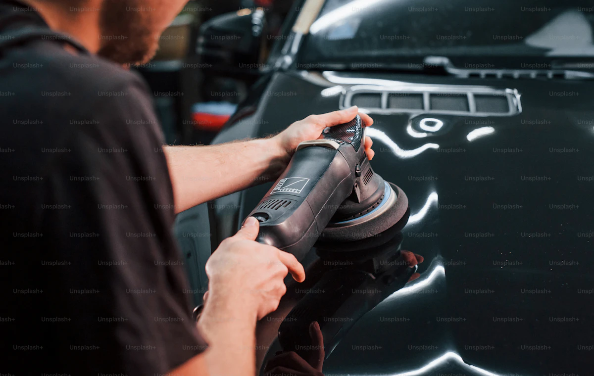 Professional detailer polishing and applying ceramic coating to a black car surface