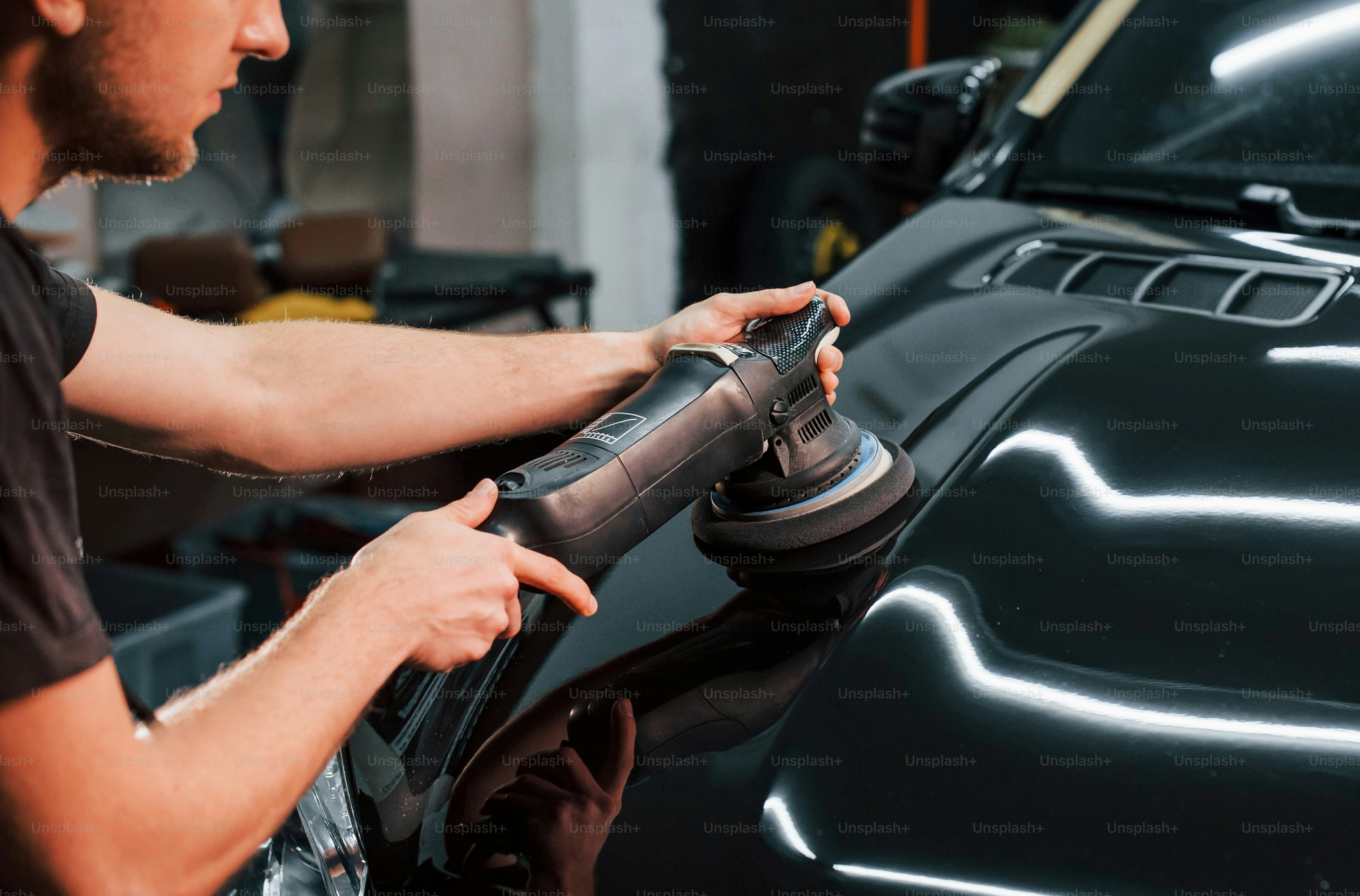 Guy polishing surface of vehicle. Modern black automobile get cleaned by man inside of car wash station.
