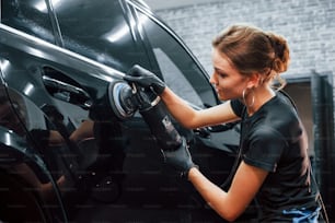 Polishing surface of vehicle. Modern black automobile get cleaned by woman inside of car wash station.