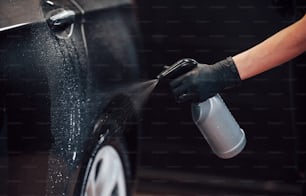 Pulvérisation du véhicule. Une automobile noire moderne est nettoyée par une femme à l’intérieur de la station de lavage de voiture.