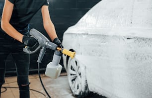 Utilizzando acqua ad alta pressione. L'automobile nera moderna viene pulita dalla donna all'interno della stazione di lavaggio dell'auto.