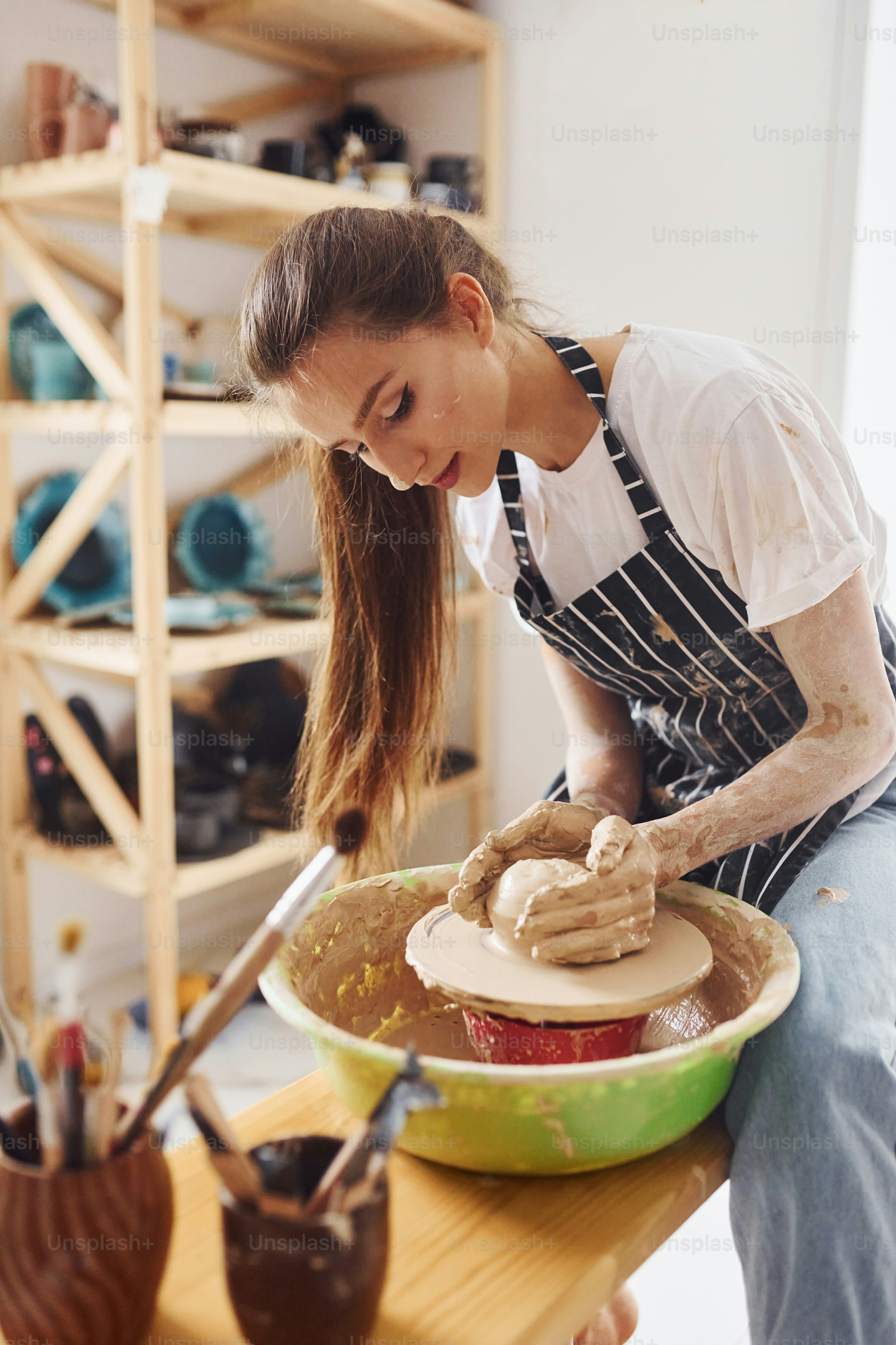 Young female ceramist working by using pottery wheel indoors and making handmade clay product.