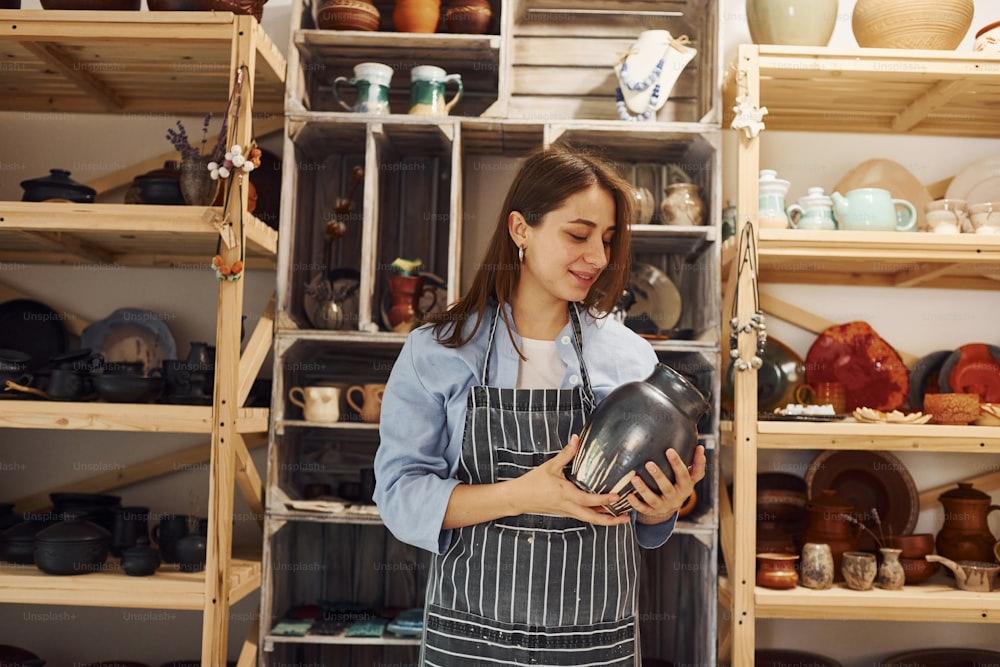 Young female ceramist indoors holding handmade clay product. Conception of pottery.