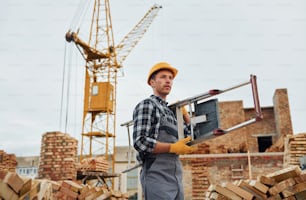 Ladder in hands. Construction worker in uniform and safety equipment have job on building.