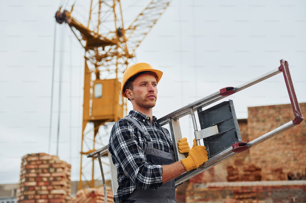 Ladder in hands. Construction worker in uniform and safety equipment have job on building.