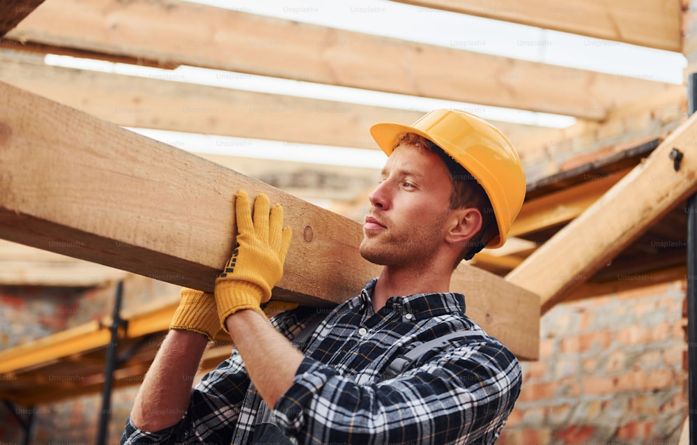 Transporting wooden boards. Construction worker in uniform and safety equipment have job on building.