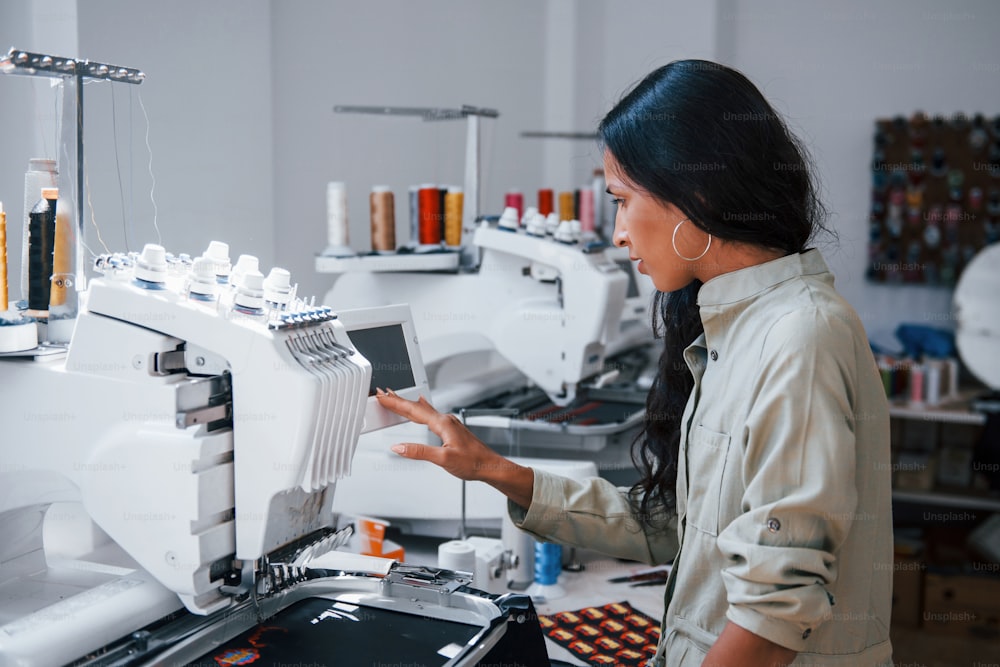 美しい女性労働者が機械のそばの縫製工場にいる。