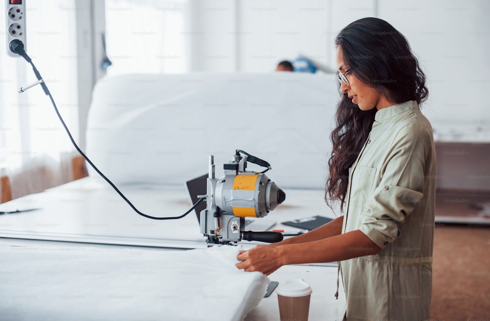 Beautiful female worker with glasses is in the sewing factory.