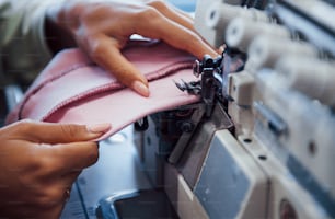 Detailed view of dressmaker woman sews clothes on sewing machine in factory.