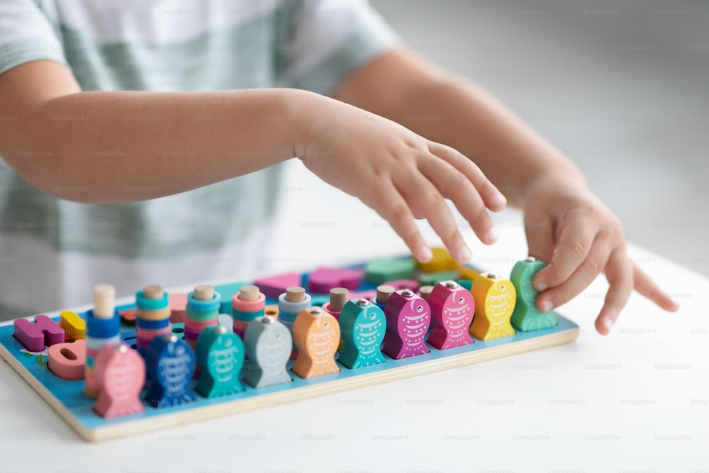 Modern eco-friendly toys. Close up shot of unrecognizable little boy playing colorful wooden fishes game, sitting at white table, empty space