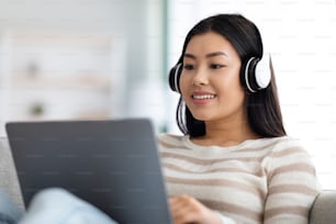 Online-Abschluss. Junge asiatische Frau in Headset-Studie mit Laptop zu Hause, Millennial-Koreanerin, die Kopfhörer trägt, schaut sich ein Webinar auf einem PC-Computer an und genießt Fernunterricht, Nahaufnahme