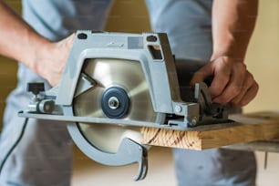 Close-up of muscular carpenter hands using new shiny modern powerful circular sharp electrical saw for cutting hard wooden board. Professional tools for construction and building concept.