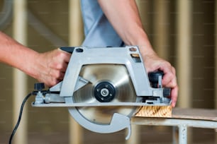 Close-up of muscular carpenter hands using new shiny modern powerful circular sharp electrical saw for cutting hard wooden board. Professional tools for construction and building concept.