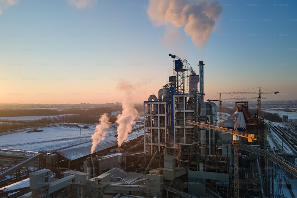 Luftaufnahme der Zementfabrik mit hoher Betonwerksstruktur und Turmdrehkran auf dem industriellen Produktionsgelände am Abend. Herstellung und globales Industriekonzept.