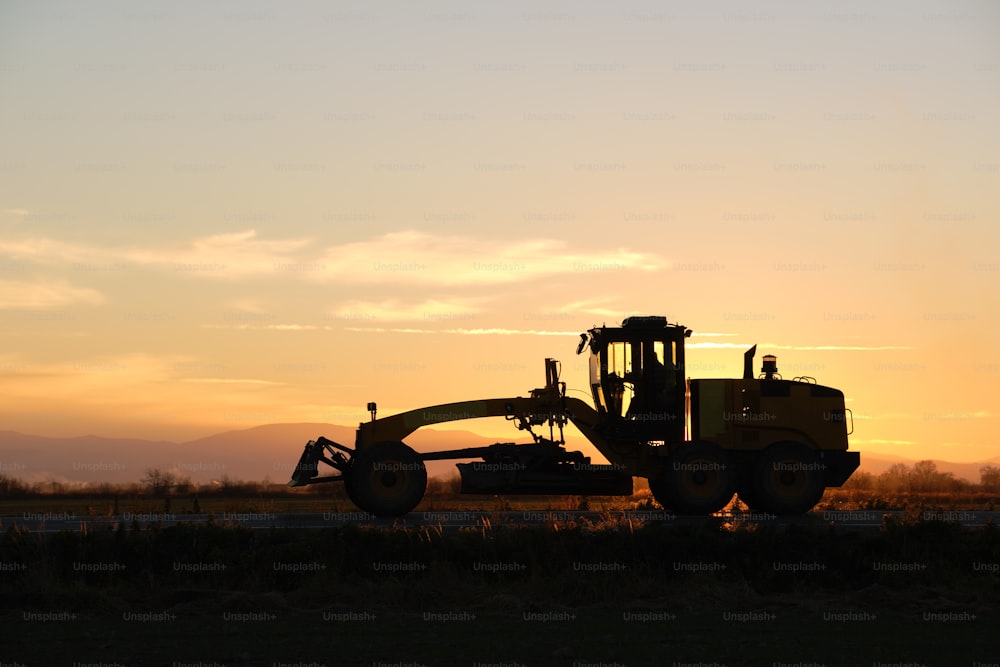 Silhouette of heavy duty tractor driving on road at sunset.