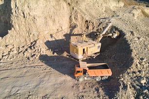 Luftaufnahme des Tagebaus von Sandsteinmaterialien für die Bauindustrie mit Bagger, der Muldenkipper mit Steinen belädt. Schweres Gerät im Bergbau und in der Produktion von nützlichen Mineralien.