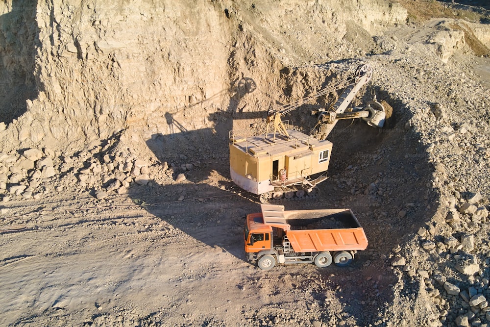 Aerial view of open pit mine of sandstone materials for construction industry with excavator loading dump truck with stones. Heavy equipment in mining and production of useful minerals concept.