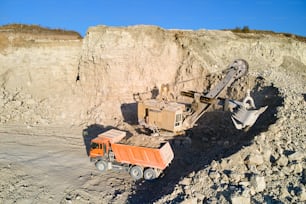 Vista aérea de mina a cielo abierto de materiales areniscos para la industria de la construcción con excavadora cargando camión volquete con piedras. Concepto de equipo pesado en minería y producción de minerales útiles.
