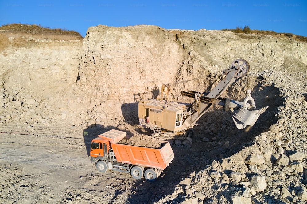 Luftaufnahme des Tagebaus von Sandsteinmaterialien für die Bauindustrie mit Bagger, der Muldenkipper mit Steinen belädt. Schweres Gerät im Bergbau und in der Produktion von nützlichen Mineralien.