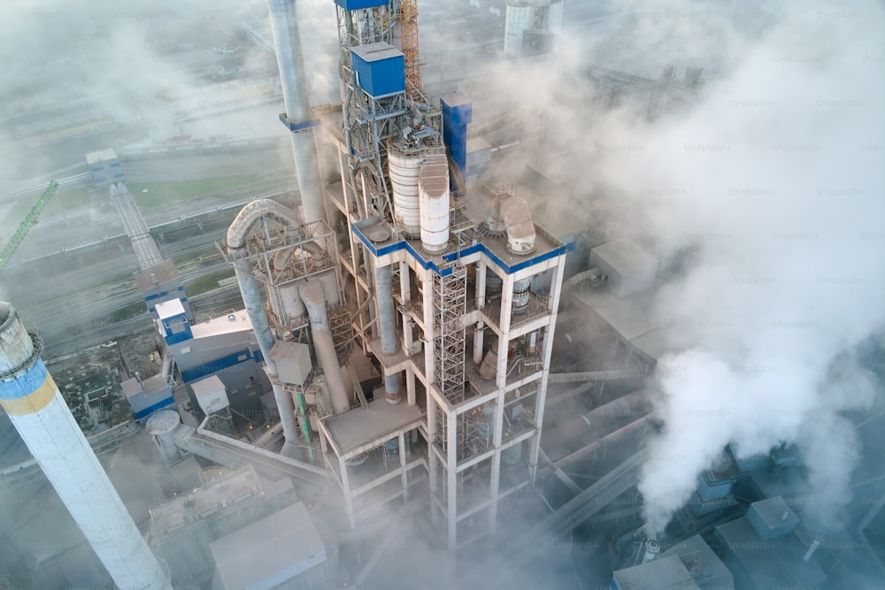霧の夕方の工業製造現場の高いコンクリートプラント構造とタワークレーンを備えたセメント工場の空撮。生産とグローバルな産業コンセプト。