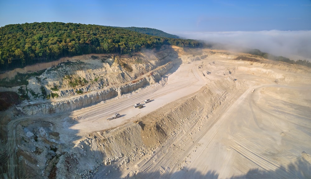 Vue aérienne d’un site minier à ciel ouvert d’extraction de matériaux calcaires pour l’industrie de la construction avec des excavatrices et des camions à benne basculante.