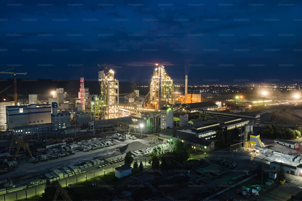 夜間の工業生産地でのコンクリート工場構造の高いセメント工場とタワークレーンの空撮。製造とグローバルな業界のコンセプト。