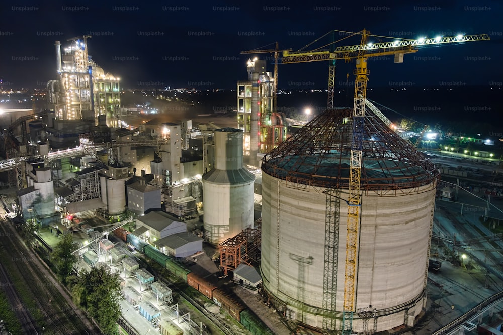 Vista aérea da fábrica de cimento com estrutura de alta planta de concreto e guindastes de torre na área de produção industrial à noite. Fabricação e conceito de indústria global.