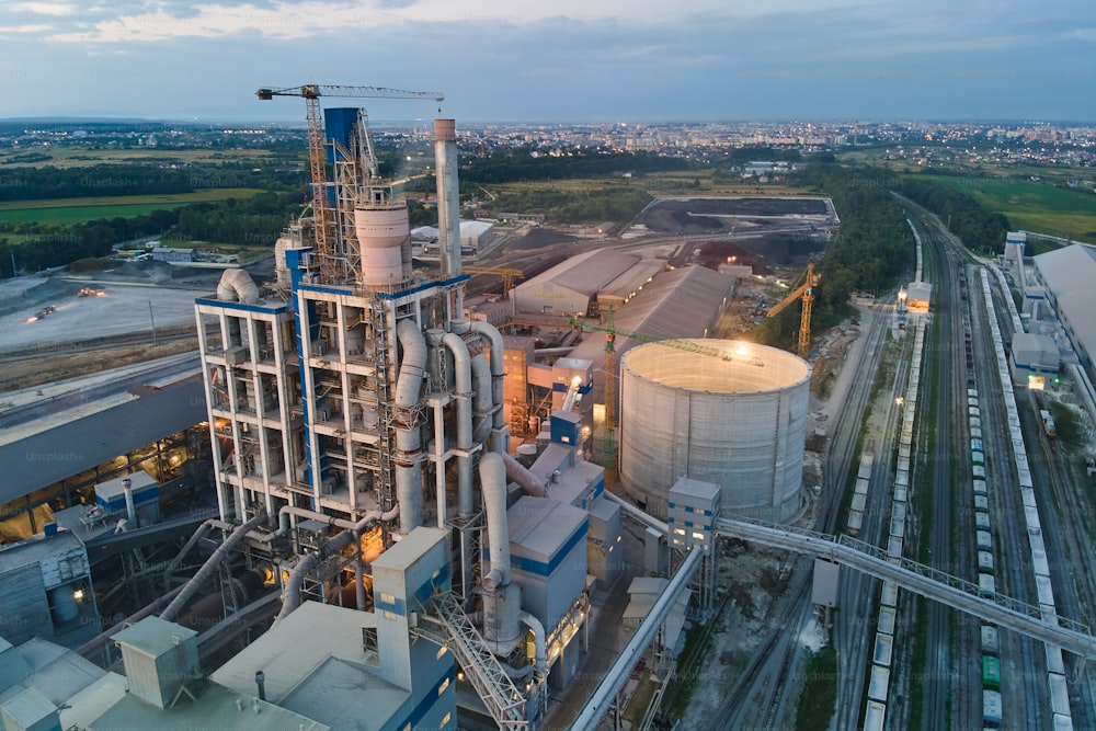 높은 콘크리트 공장 구조가 있는 시멘트 공장과 야간에 산업 생산 지역에 있는 타워 크레인의 조감도. 제조 및 글로벌 산업 개념.