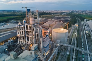 Aerial view of cement factory with high concrete plant structure and tower cranes at industrial production area at night. Manufacture and global industry concept.