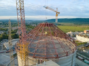 Aerial view of cement factory under construction with high concrete plant structure and tower crane at industrial production area. Manufacture and global industry concept.