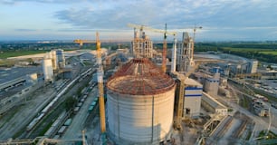 Luftaufnahme der im Bau befindlichen Zementfabrik mit hoher Betonwerksstruktur und Turmdrehkranen im industriellen Produktionsbereich. Herstellung und globales Industriekonzept.