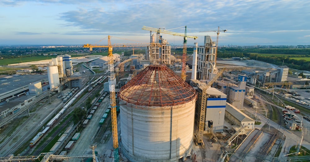 工業生産地の高いコンクリートプラント構造とタワークレーンを備えた建設中のセメント工場の空撮。製造とグローバルな業界のコンセプト。