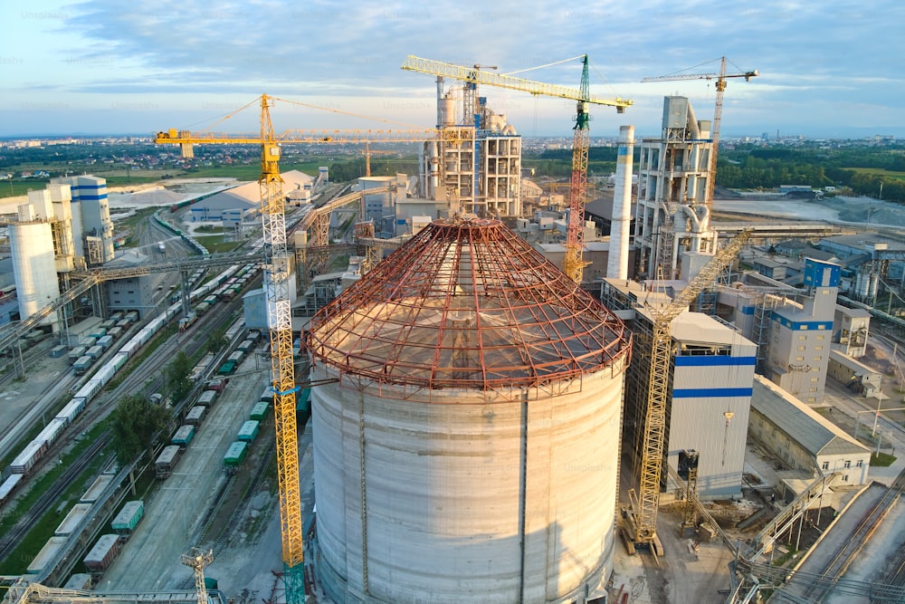 工業生産地の高いコンクリートプラント構造とタワークレーンを備えた建設中のセメント工場の空撮。製造とグローバルな業界のコンセプト。