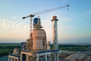 Aerial view of cement factory with high concrete plant structure and tower crane at industrial production site. Manufacture and global industry concept.