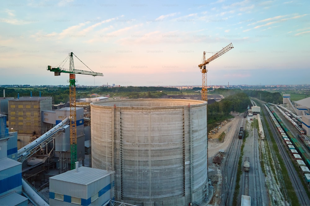 Cement plant with high factory structure and tower cranes at industrial production area. Manufacture and global industry concept.