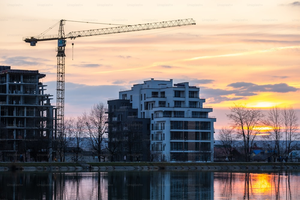 Tower crane and high residential apartment buildings under construction on lake shore. Real estate development.