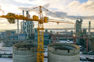 Aerial view of cement plant with high factory structure and tower crane at industrial production area.