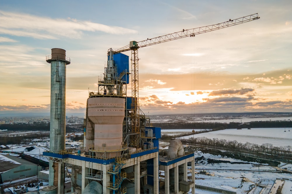 Aerial view of cement plant with high factory structure and tower crane at industrial production area.