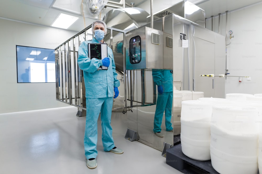 Un travailleur médical en combinaison de laboratoire bleue se tient près de grosses machines en acier