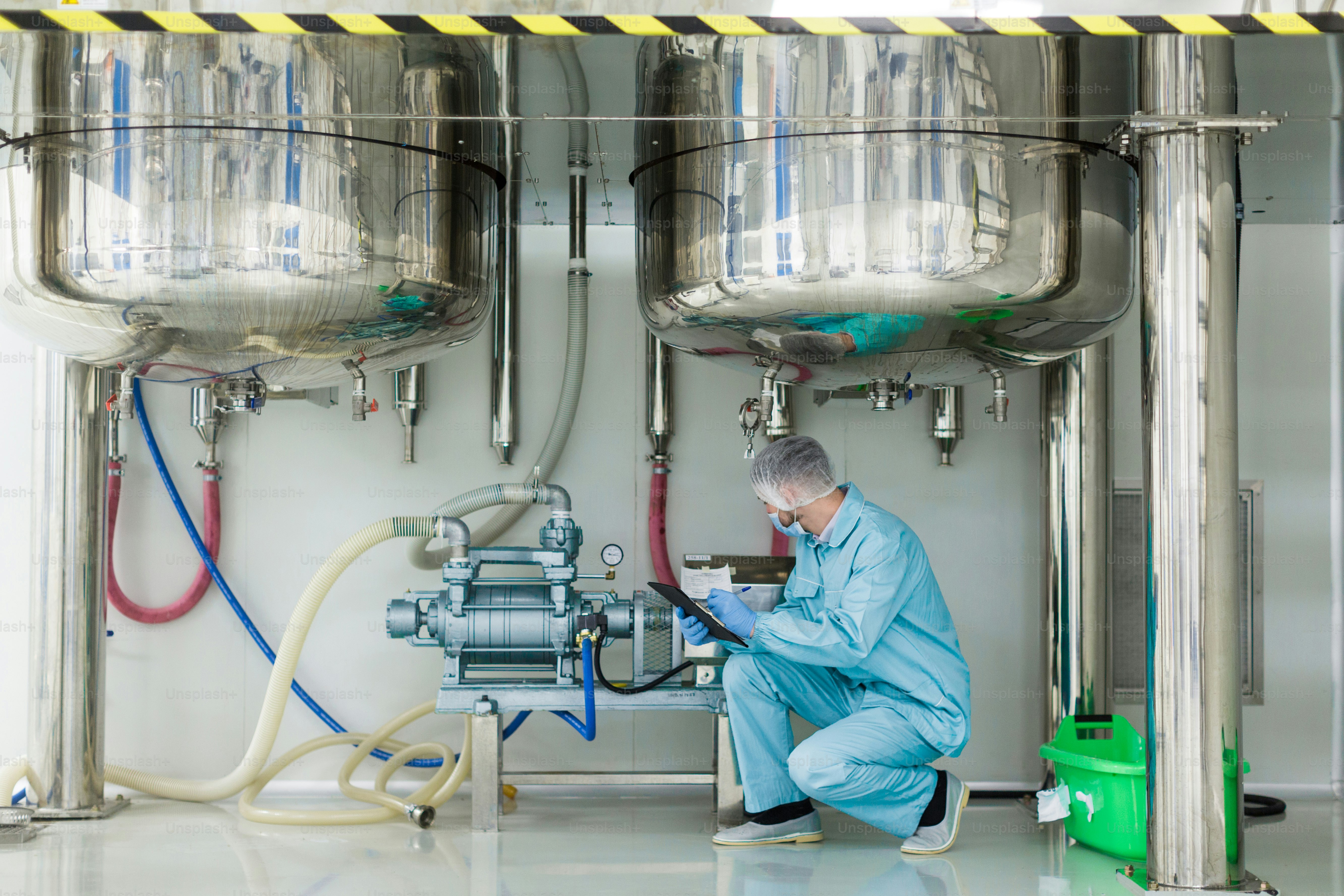 Scirntist in tuta da laboratorio blu controlla il motore sotto due serbatoi cromati