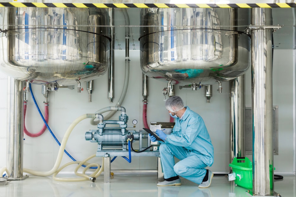scirntist em motor de verificação de terno de laboratório azul sob dois tanques cromados