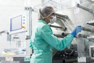 Científico caucásico doblado en traje de laboratorio azul trabaja con máquina de fabricación con ejes