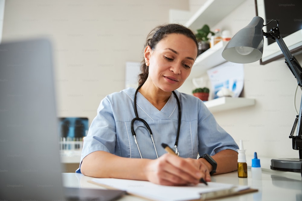 Trabajadora médica tomando notas en una página de cuaderno sentada en el escritorio de su oficina