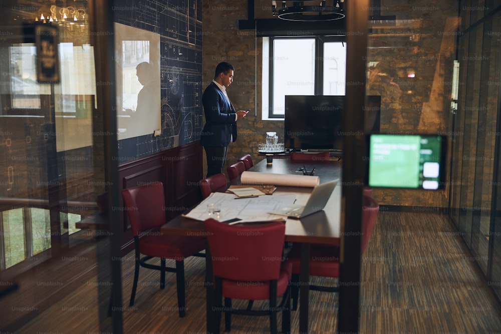 Side view of a concentrated businessman with a gadget in his hand standing by the window