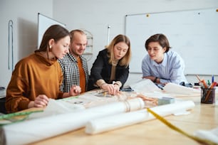 Calm fashion designer using a ruler on the garment pattern and friendly smiling colleagues watching her working