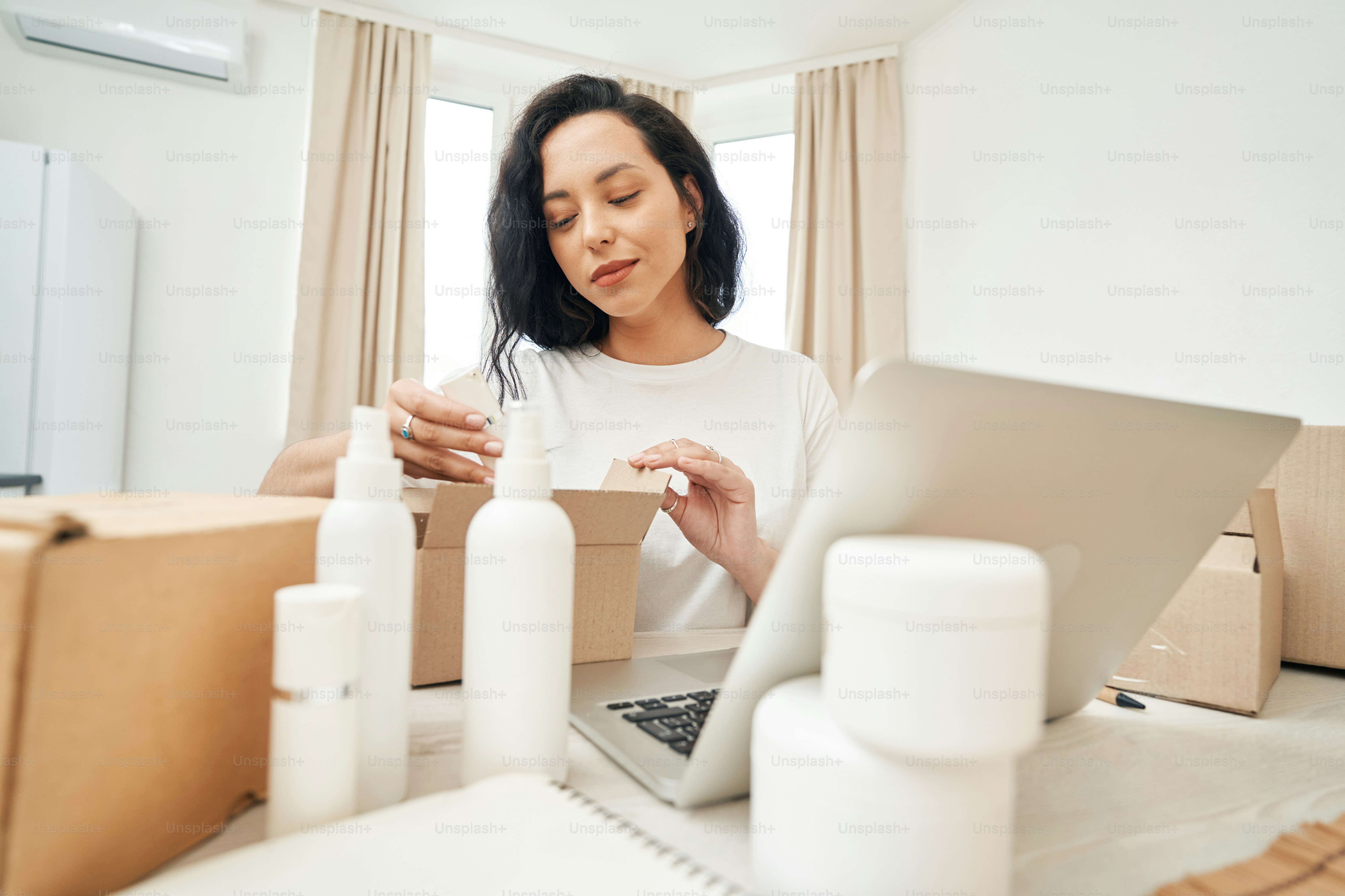 Focused woman sitting at table and putting beauty product into open cardboard box