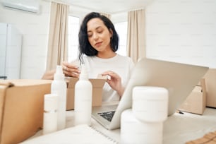 Focused woman sitting at table and putting beauty product into open cardboard box
